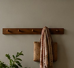 A hand-woven scarf hanging from a walnut peg rail above a stoneware vase.
